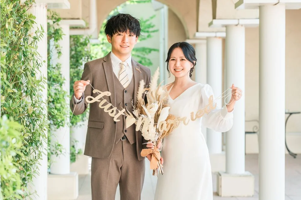 「Just Married」のガーランドとドライフラワーのブーケを手に微笑む男女